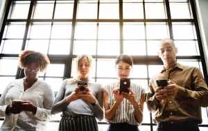 four people using smartphones behind glass wall
